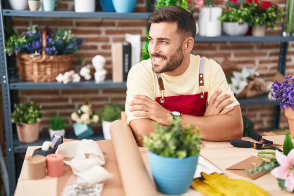 Young hispanic man florist smiling confident sitting with arms crossed gesture at florist