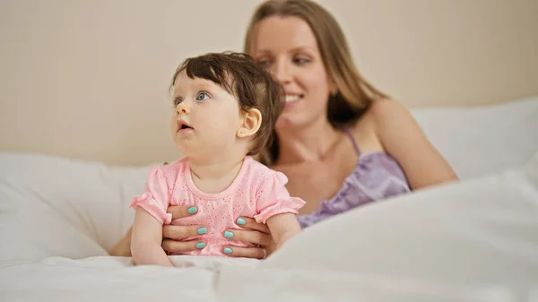 Mother and daughter sitting on bed smiling at bedroom
