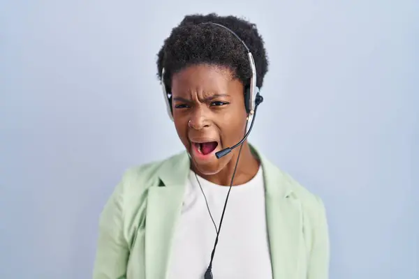 African american woman wearing call center agent headset angry and mad screaming frustrated and furious, shouting with anger. rage and aggressive concept.