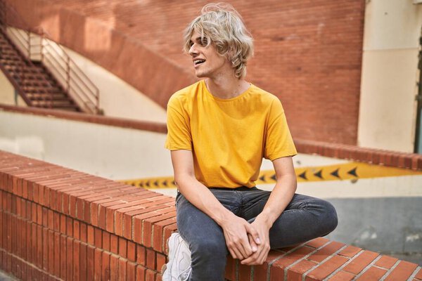 Young blond man looking to the side sitting on bench at street