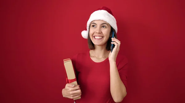 Młoda Piękna Latynoska Kobieta Świątecznym Kapeluszu Rozmawia Smartfonie Trzymając Prezent — Zdjęcie stockowe