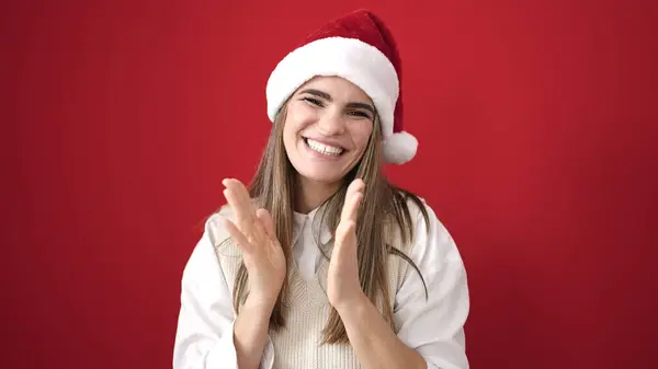 惊慌失措 头戴圣诞礼帽的女人在孤零零的红色背景上拍手 — 图库照片