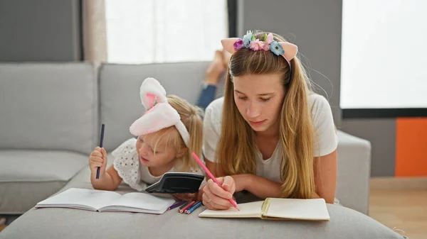 Caucasian mother and daughter lying on sofa drawing on notebook at home
