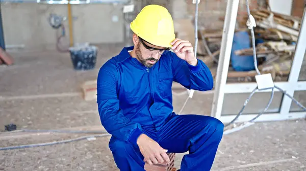 Young hispanic man worker sitting on brick tired at construction site