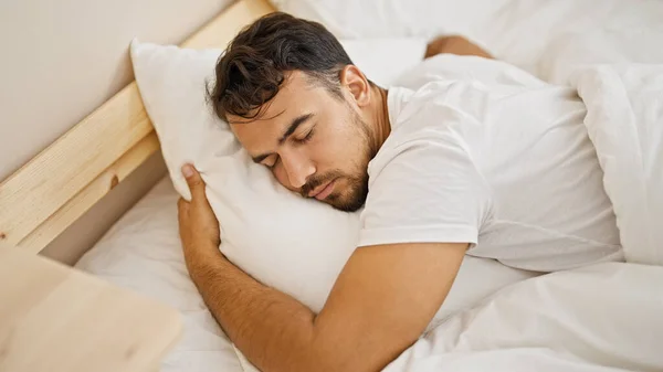 Young hispanic man hugging pillow lying on bed sleeping at bedroom