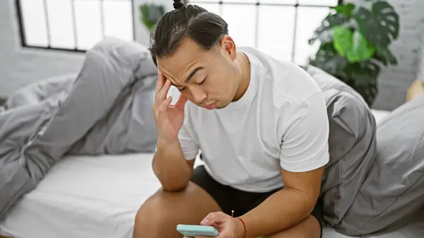 Стресс Молодой Китаец Сидит Спальне Используя Смартфон Испытывая Серьезный Стресс — стоковое фото