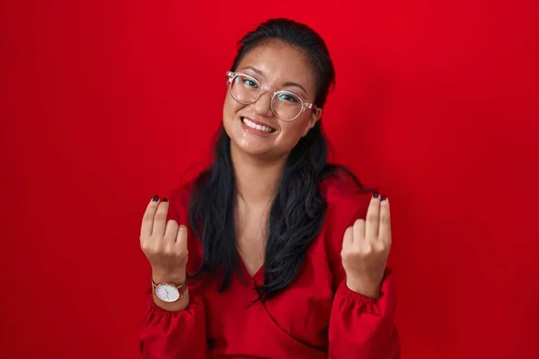 アジアの若い女性は 手でお金のジェスチャーをする赤い背景の上に立って 給与の支払いを求める 億万長者のビジネス — ストック写真