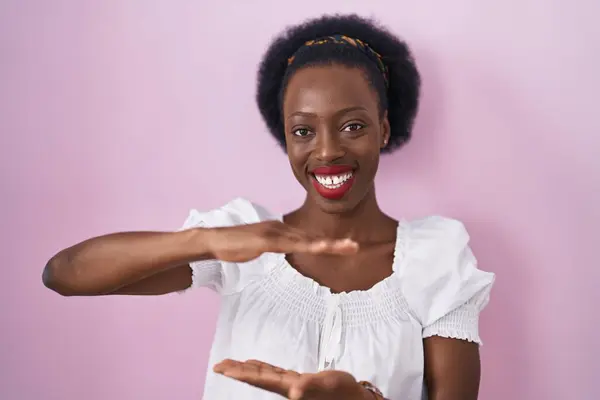非洲女人 卷曲的头发 站在粉色的背景上 手举着大而大的标志 测量符号 微笑着看着摄像机 计量概念 — 图库照片