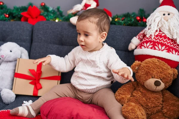 Uroczy Latynoski Maluch Trzyma Świąteczny Prezent Siedząc Kanapie Domu — Zdjęcie stockowe