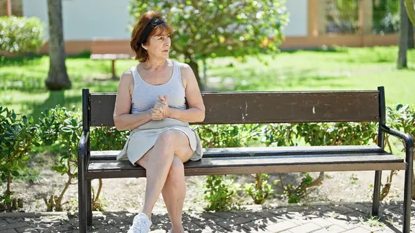 中年女性座っていますベンチ一人で周りを見回す公園 — ストック写真