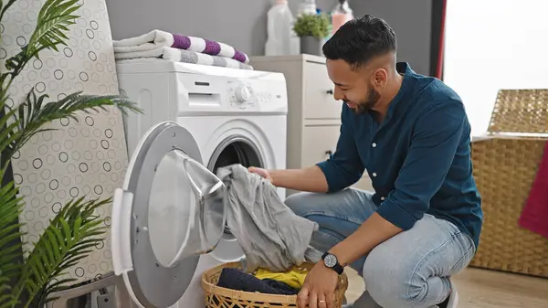 Young hispanic man doing laundry with washing machine at laundry room