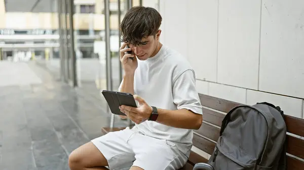 スマートな若いヒスパニック系のティーンエイジャーは 彼のスマートフォンとタッチパッドを使用して深刻な電話会話に深く魅了され キャンパスで気軽に屋外に座りました — ストック写真