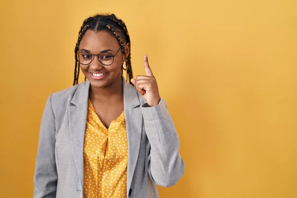 非洲裔美国妇女 头戴辫子 站在黄色的背景上 带着第一指尖 面带微笑 自信而快乐 — 图库照片