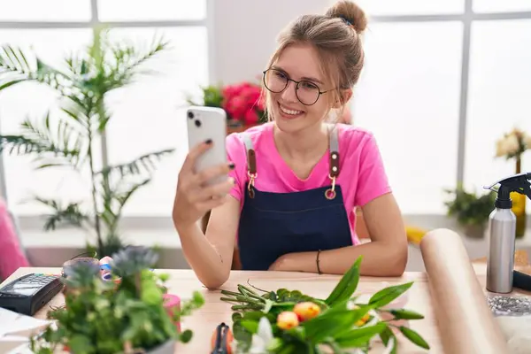 Çiçekçide kendine güvenen genç sarışın kadın akıllı telefondan selfie çekiyor.