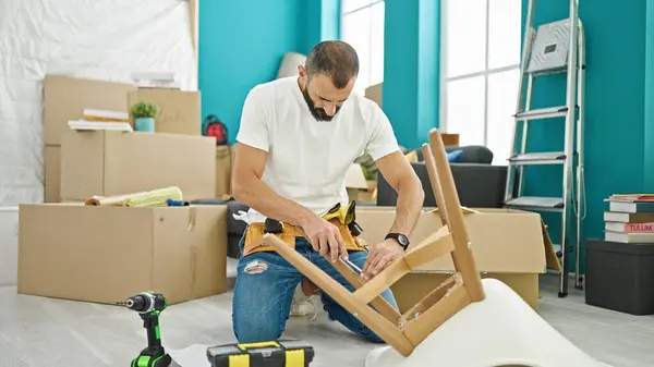 Young hispanic man repairman repairing chair using screwdriver at new home