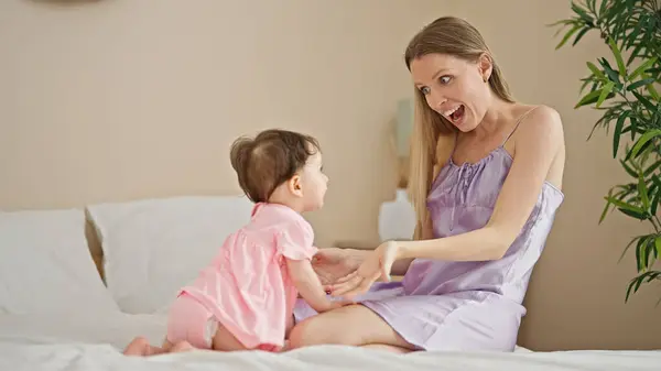 Mother and daughter sitting on bed surprised at bedroom