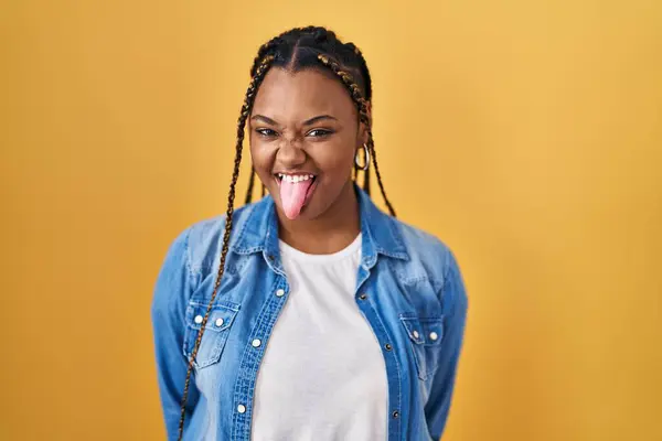 African American Woman Braids Standing Yellow Background Sticking Tongue Out — Zdjęcie stockowe