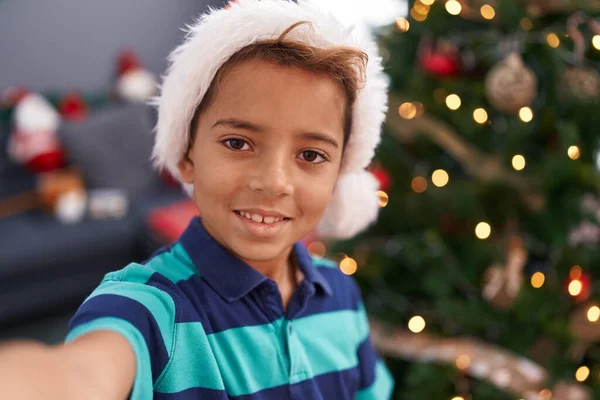 愛らしいヒスパニックの少年は自宅でクリスマスツリーで立っているカメラでセルフィーを作ります — ストック写真