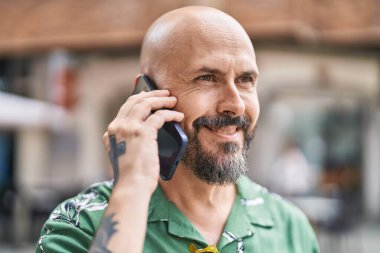 Genç kel adam gülümsüyor. Kendine güveni tam. Akıllı telefondan konuşuyor.