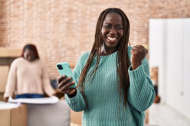 Yeni evinde akıllı telefon kullanan Afrikalı bir kadın gururla bağırıyor, zaferi kutluyor ve kollarını kaldırarak başarıyı kutluyor. 