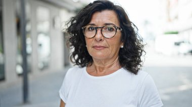 Middle age hispanic woman standing with serious expression at street