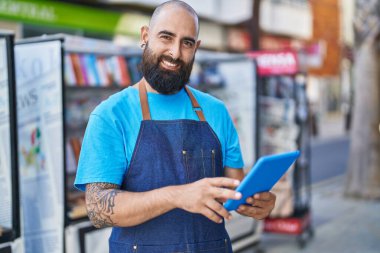 Young bald man waiter smiling confident using touchpad at coffee shop terrace