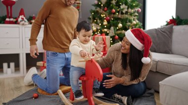 Çift ve oğul evde ren geyikleriyle oynuyorlar Noel ağacında sallanıyorlar.