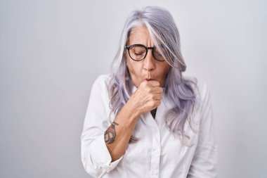 Beyaz arka planda duran gözlüklü orta yaşlı bir kadın kendini iyi hissetmiyor ve soğuk algınlığı veya bronşitin belirtisi olarak öksürüyor. sağlık hizmeti kavramı. 