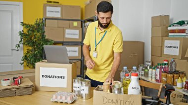 Genç İspanyol gönüllü yardım merkezinde dizüstü bilgisayar kullanarak ürünleri kontrol ediyor.