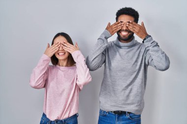 Genç İspanyol çift yan yana durup, neşeli ve komik gülümseyen elleriyle gözlerini kapatıyor. kör kavram. 