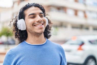 Young latin man smiling confident listening to music at street