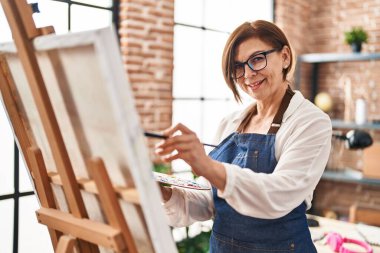 Sanat stüdyosunda kendine güvenen orta yaşlı kadın sanatçı gülümsüyor.
