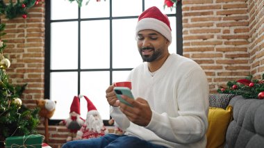 Afrika kökenli Amerikalı adam akıllı telefon kullanıyor evde Noel 'i kutlamak için kahve içiyor.