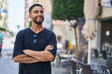 Sokakta kollarını kavuşturmuş genç bir Arap adam.