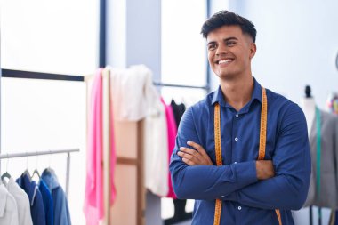 Genç İspanyol terzi gülümsüyor. Giysi fabrikasında kollarını kavuşturmuş duruyor.