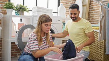 Man and woman couple smiling confident washing clothes at laundry room