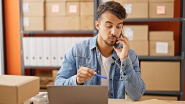 İspanyol asıllı genç iş adamı bilgisayarını kullanarak ofiste akıllı telefon tartışması yapıyor.