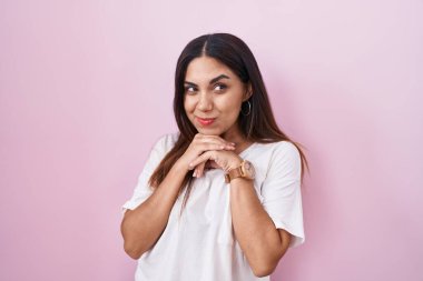 Pembe arka planda duran genç Arap kadın. Gergin ve heyecanlı. Elleri çenesinde yan tarafa bakıyor. 