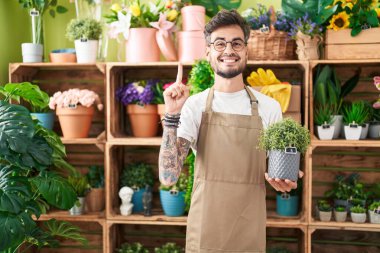 Çiçekçi dükkanında çalışan, elinde çiçeklerle gülümseyen, gülümseyen, mutlu yüzlü İspanyol dövmeli genç adam. 