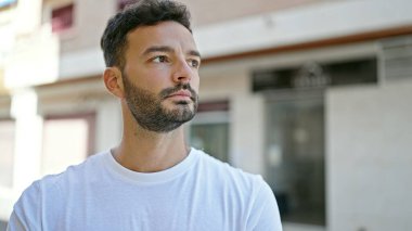 Latin kökenli genç adam ciddi bir ifadeyle sokağa bakıyor.