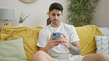 Evdeki kanepede oturan, akıllı telefon kullanan genç bir İspanyol.