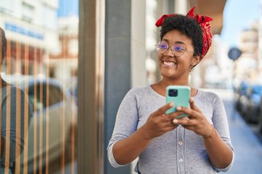 Afro-Amerikalı kadın sokakta akıllı telefon kullanarak kendine güveniyor.