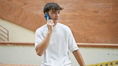 Gündüz Latin kökenli genç bir erkek, güneşli bir şehir sokağında ciddi bir telefon konuşmasına dalmış, havalı bir ifadeyle genç bir adamın hayat tarzı portresi, açık havada akıllı telefonuyla tutkuyla konuşuyor.