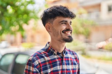 Young hispanic man smiling confident looking to the side at street