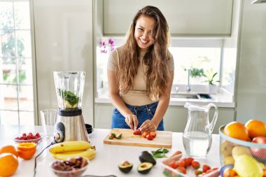 Genç ve güzel İspanyol kadın mutfakta çilek doğrayan blender ile sebze suyu hazırlıyor.