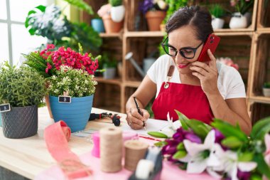 Çiçekçide defterine dokunmatik yazı yazan güzel İspanyol bir çiçekçi.