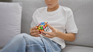 Kanepede oturan sarışın çocuk evde rubik küple oynuyor.
