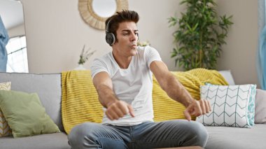 Genç İspanyol adam evde kanepede oturmuş müzik dinliyor.