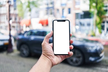 Akıllı telefon tutan adam araba parkında beyaz boş ekran gösteriyor.