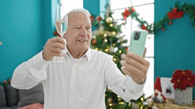 Evde elinde şampanya kadehiyle Noel 'i kutlayan yaşlı, kır saçlı adam.